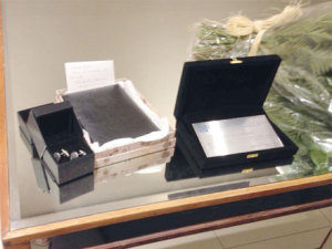 A placa de prata em homenagem, à direita. Entre os presentes, à esquerda, par de abotoaduras, também em prata, com desenhos de pinhões